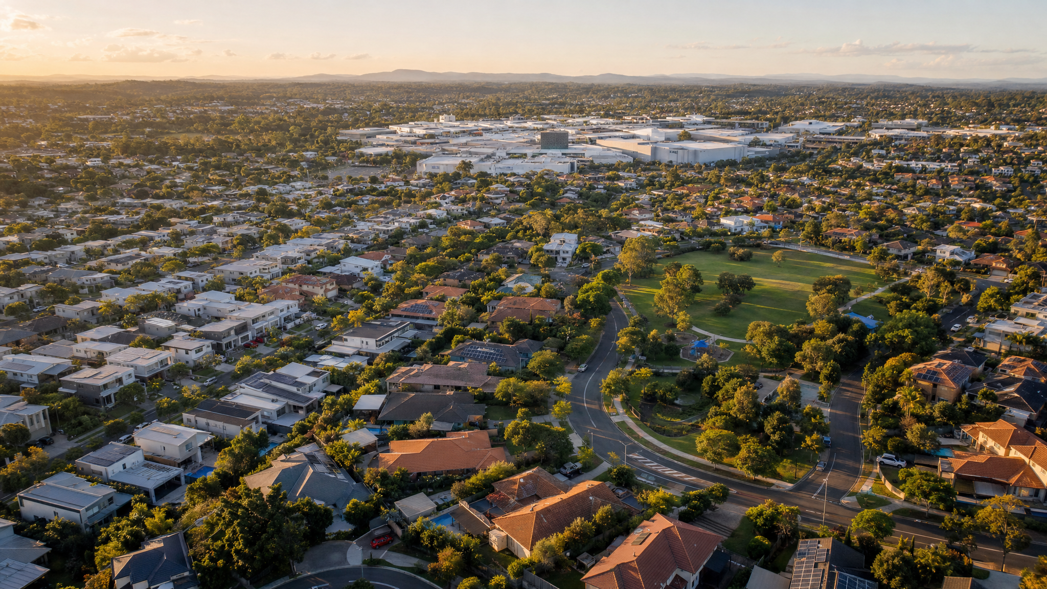Aerial view of Carindale, Brisbane, modern eastern suburb with family homes, curving streets, parks and a large shopping centre complex on the horizon